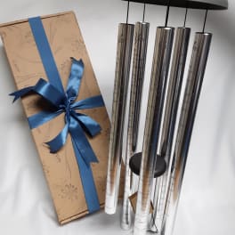 Gift box with blue ribbon beside a set of silver wind chimes