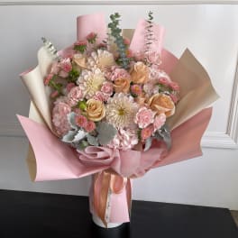 Pink and peach bouquet with roses, chrysanthemums, and carnations in pastel wrap