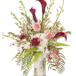 Tall bouquet of burgundy calla lilies and pink flowers in a glass vase