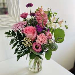 Mixed bouquet of pink and purple flowers with white accents in a clear glass jar vase