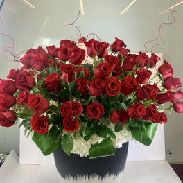 Large arrangement of red roses and white flowers in a black and white ceramic pot