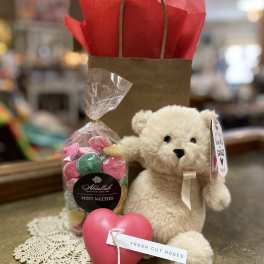 Gift set with teddy bear, bag of candies, and pink heart on a lace doily