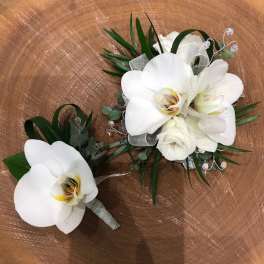 White orchid corsage and matching boutonniere with ribbon accents on a wooden surface