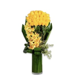 Tall arrangement of yellow roses and orchids in a green-lined glass cylinder vase