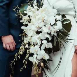 Cascading bridal bouquet of white orchids held by a bride in a white dress