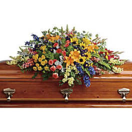 Large multicolor casket spray of mixed flowers arranged atop a wood coffin