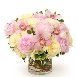 Low arrangement of pink peonies, pale orchids, and cream roses in a clear glass vase.