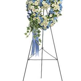 Heart-shaped blue and white sympathy wreath on a metal easel with trailing ivy and blue ribbon.
