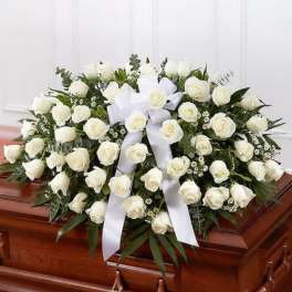White rose casket spray with large bow on a wooden casket