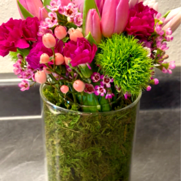 Pink tulips and magenta flowers arranged in a clear glass vase