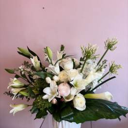 White floral arrangement in a white vase with lilies and roses