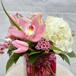 Low pink and white flower arrangement with orchid, tulips, roses, and hydrangea in a pink glass cube vase.
