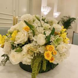 White and yellow floral centerpiece in a low round container