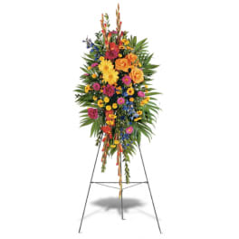 Tall standing spray of bright yellow, orange, and pink flowers with blue accents on a metal easel