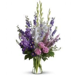 Tall arrangement of purple and white flowers with lavender roses in a clear glass vase