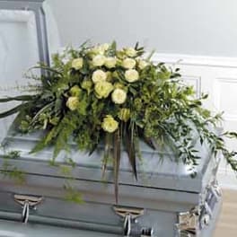 White rose casket spray with trailing greenery on a gray casket