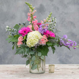 Mixed pink, purple, and white flowers in a glass vase beside a small candle holder.