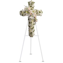 Standing floral cross of white blooms with lilies and roses on a white easel