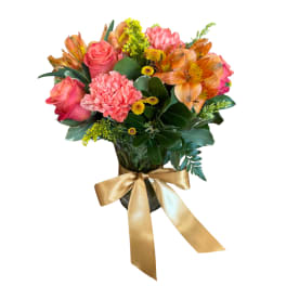 Bouquet of pink roses, carnations, and orange alstroemeria in a vase with a gold ribbon