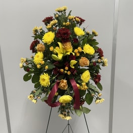 Standing floral spray with yellow and burgundy flowers on an easel
