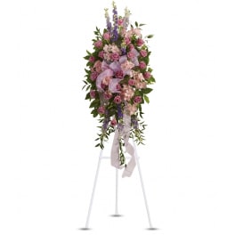 Tall standing spray of pink and lavender flowers with ribbon on a white easel stand