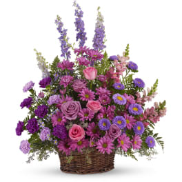 Fan-shaped basket arrangement of pink and purple roses, daisies, carnations, asters, and delphinium.
