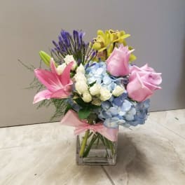Mixed bouquet of pink lilies, roses, hydrangea, and orchids in a glass vase