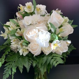White roses and alstroemeria in a glass vase with fern foliage