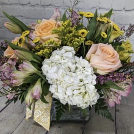Mixed bouquet with peach roses, white hydrangea, and yellow accents in a glass vase