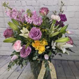 Mixed bouquet of roses, lilies, and purple blooms in a glass vase
