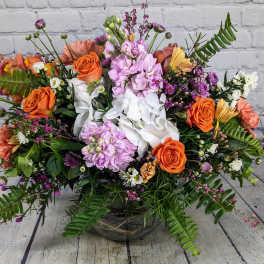 Mixed bouquet of orange and pink flowers in a low glass vase