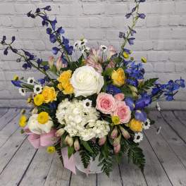 Mixed bouquet with roses, hydrangea, and blue delphinium in a white container