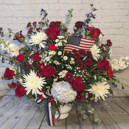 Large red, white, and blue floral arrangement in a white vase with an American flag