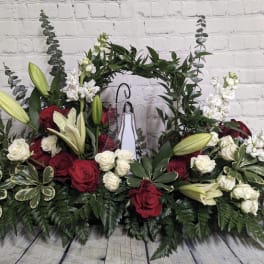 Symmetrical floral arrangement with red and white roses, lilies, and greenery around a central cross