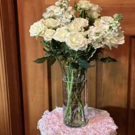 White roses and small white flowers arranged in a clear glass vase