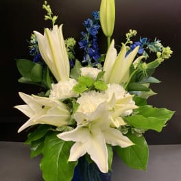White lilies and blue flowers arranged in a blue vase