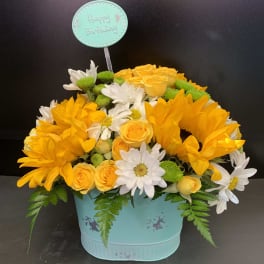 Yellow roses and white daisies in a turquoise birthday container