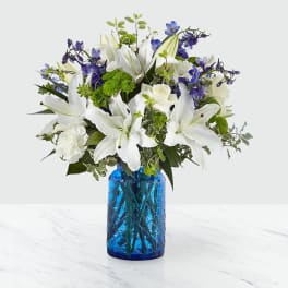 White lilies and blue flowers arranged in a blue glass vase