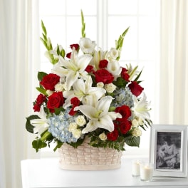 Basket arrangement of red roses, white lilies, and blue hydrangeas
