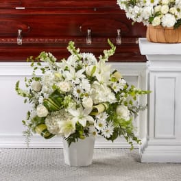 White floral arrangement in a vase beside a casket