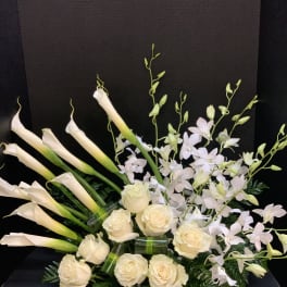 Cream calla lilies, roses, and pale orchids in a low black container