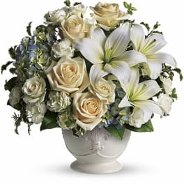 Cream roses and white lilies arranged in a white vase
