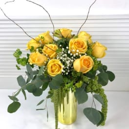 Yellow roses in a gold vase with trailing greenery
