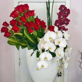Red roses and white orchids arranged in a white vase with purple orchids