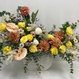 Mixed floral arrangement in a white rectangular vase with yellow and peach blooms