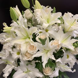 White lilies and roses arranged in a vase with daisies