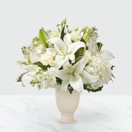 White lilies and roses arranged in a cream vase