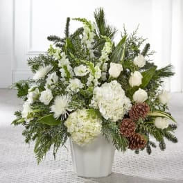 White floral arrangement in a white vase with pinecones and evergreen accents