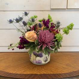 Mixed bouquet in a decorative tin container with purple, peach, and green flowers