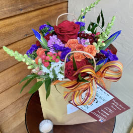 Mixed bouquet of red, orange, purple, and blue flowers in a gift bag